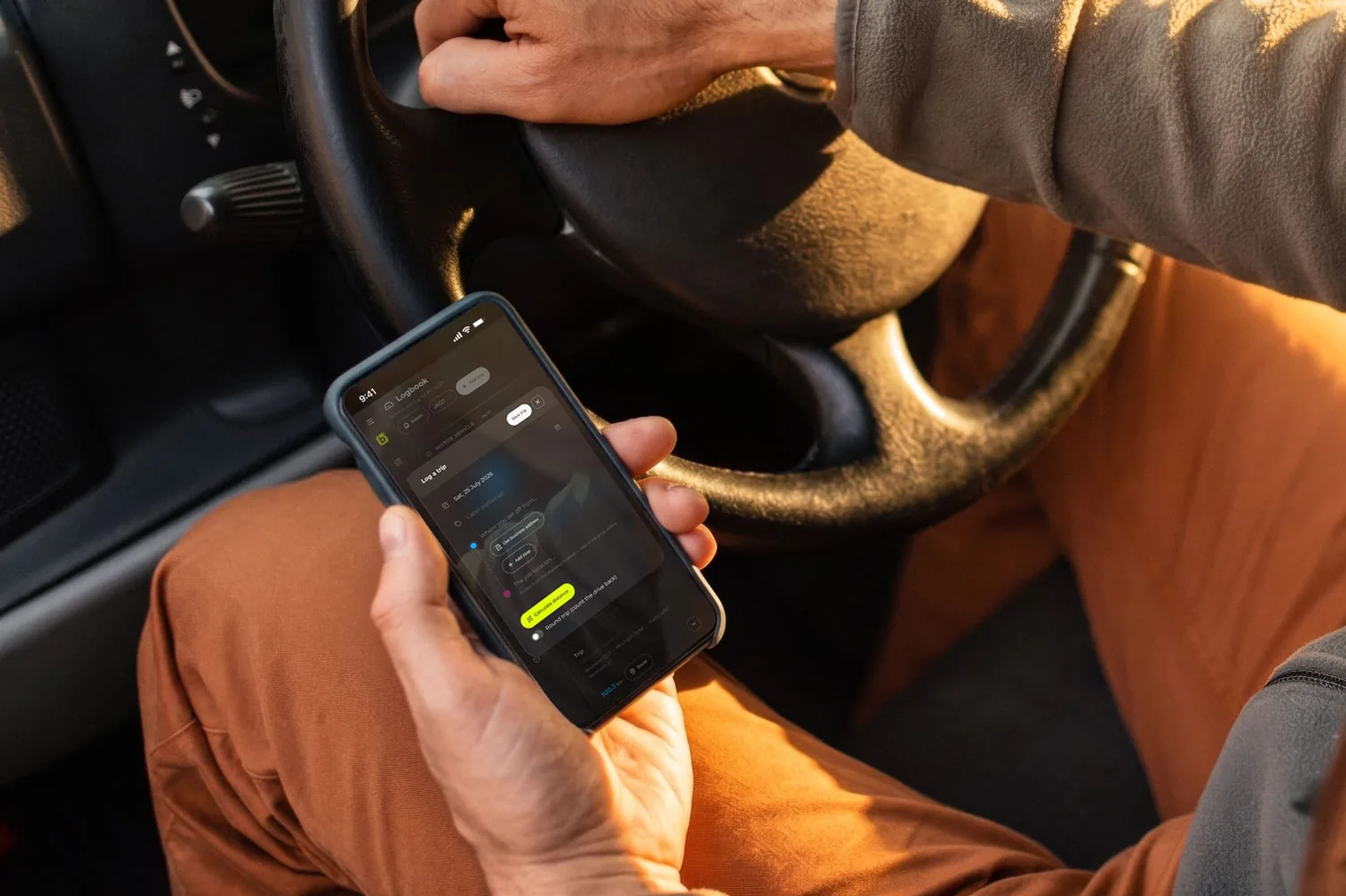 A driver in the front seat logging a trip in billed on their phone, one hand still on the steering wheel